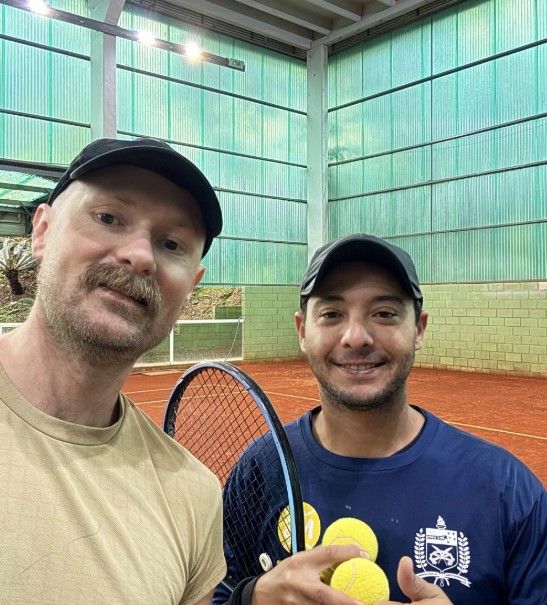 Rafael e um aluno numa quadra coberta de saibro, com bolas de tênis na mão