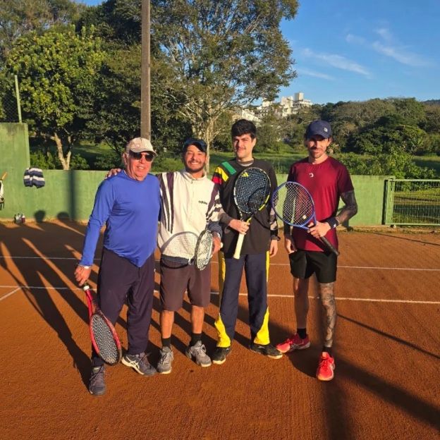 Rafael com três alunos, de raquete na mão, numa quadra de saibro no fim da tarde